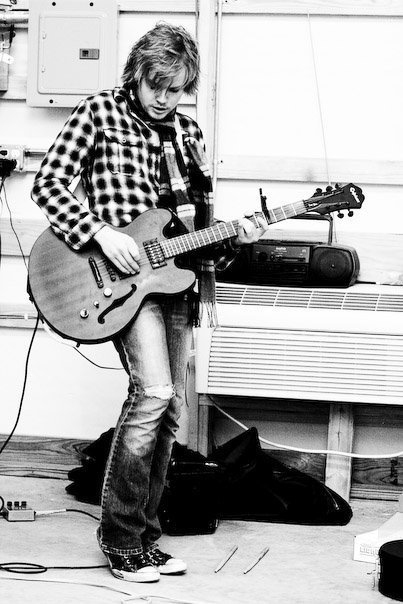 A black and white photo of a man in a plaid shirt playing an electric guitar.