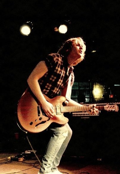 A person playing an electric guitar on stage, only their torso and guitar are visible.